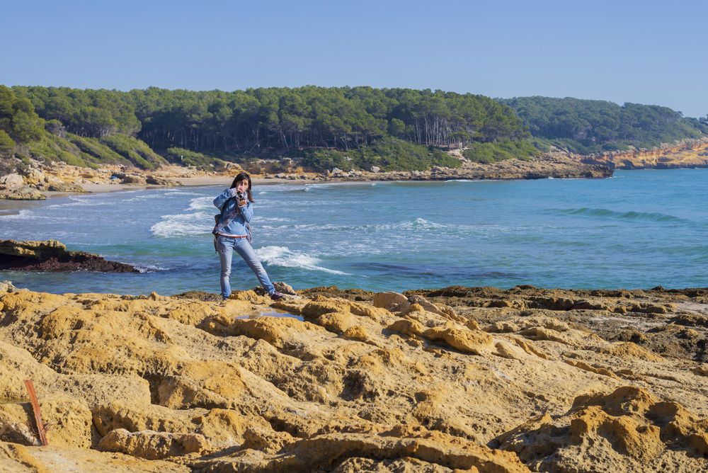 Female dressed in blue standing on rocks on coast taking picture