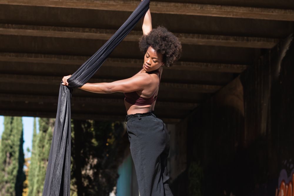 Black woman doing yoga with aerial silks in city