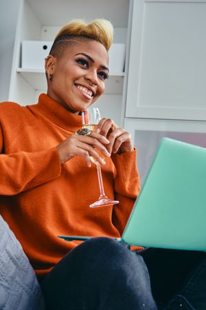 Black woman with a champagne flute looking away from her laptop