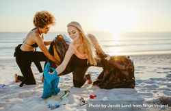 Young female surfers collecting trash in garbage bags from the beach 482vX0
