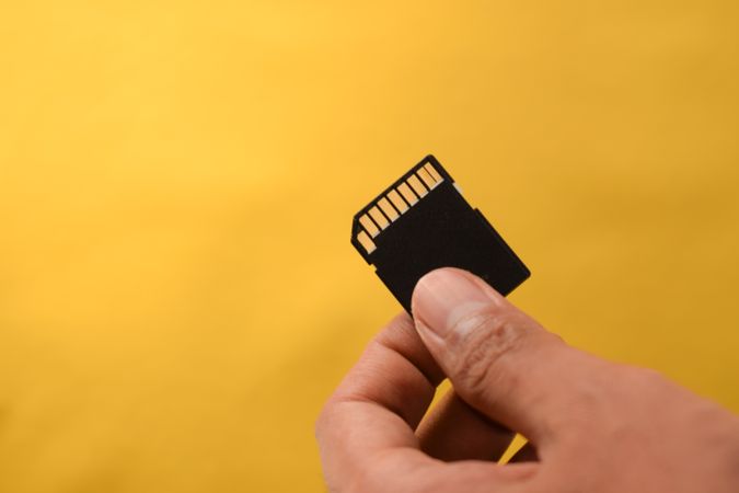 Hand holding SD card for data with yellow background with copy space