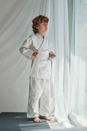 Pensive boy in kimono standing near window