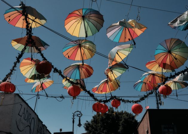 Rainbow umbrellas and red lanterns hung up on lines over street in Barrio Chino