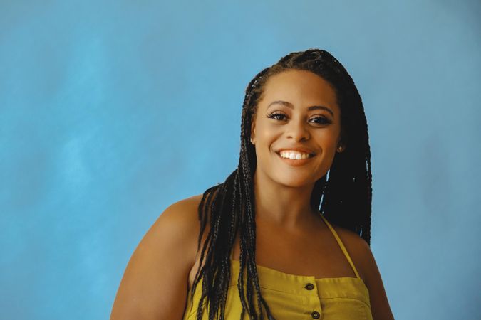 Portrait of confident smiling female with long braided hair in yellow shirt, copy space