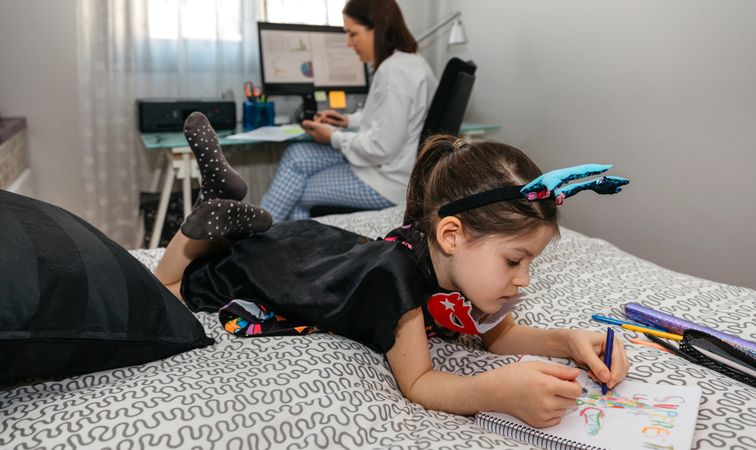 Girl drawing in disguise while her mother teleworking