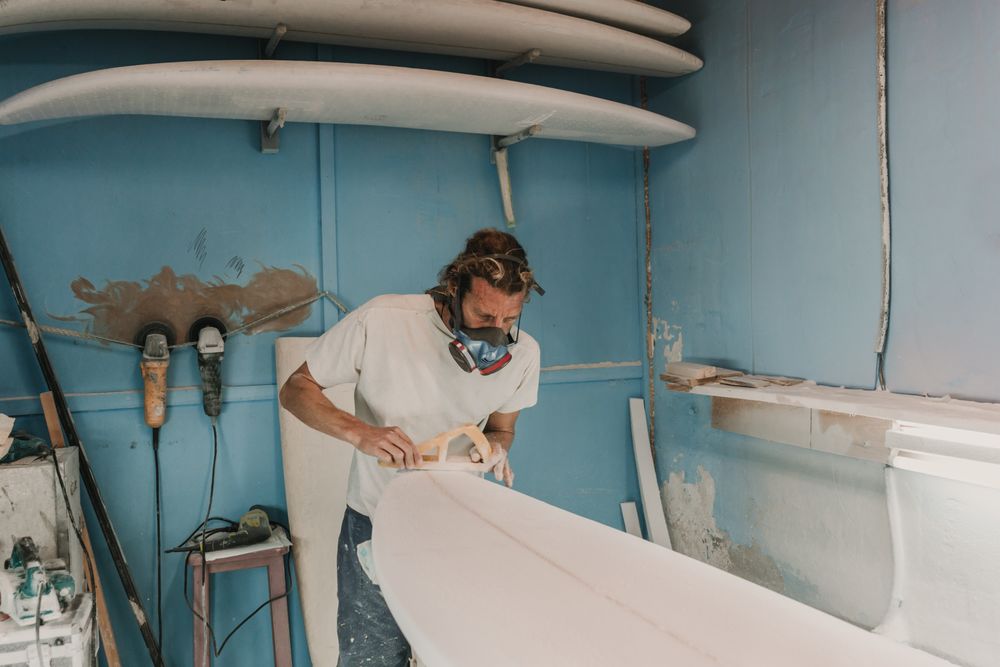 Man in respirator polishing surf board in workshop