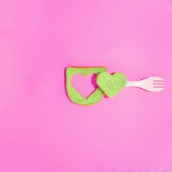Green toast with heart cut out on a pink background with fork