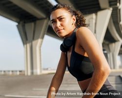 Woman under a bridge in athletic gear and headphones bEMxob