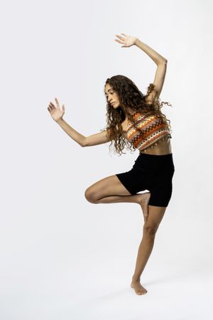 Graceful Young Woman with Curly Hair Balancing Yoga Pose in Crop Top