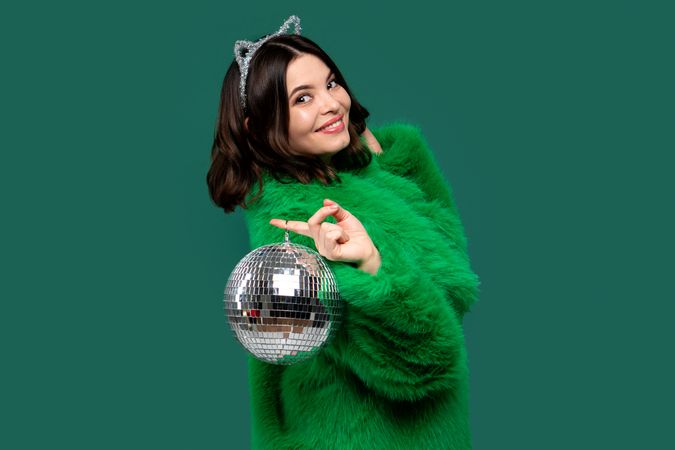 Elegant woman in green fur coat posing with disco ball.
