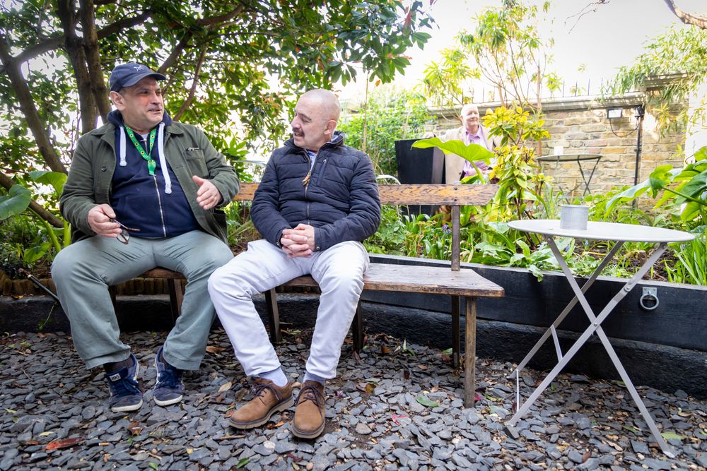 Two mature male friends talking outside on a park bench