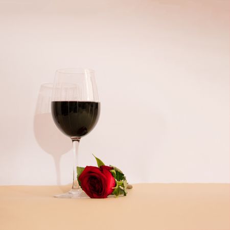 Glass of red wine with rose laying beside it