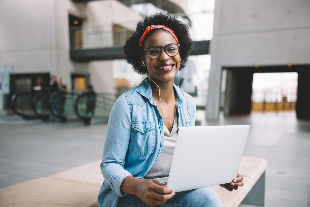 Smiling woman with laptop in atrium of building