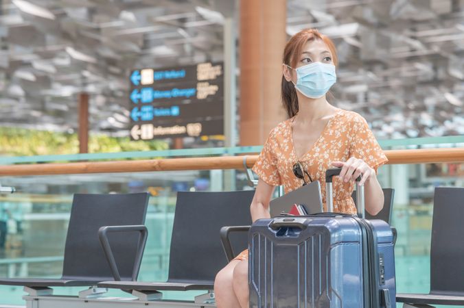 East Asian woman with facemask sitting on chair at the airport