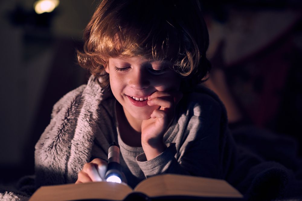 Positive boy reading book in darkness