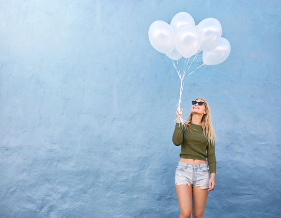 Happy young woman with bunch of balloons against blue wall