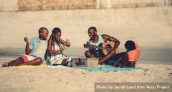 Young man playing guitar for friends at picnic on the coast 4Mx8k5