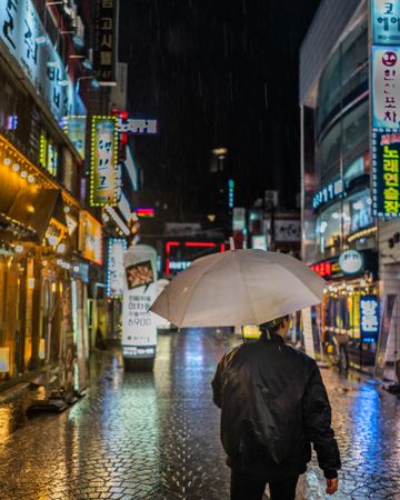 Back view of man holding umbrella walking on street during night time
