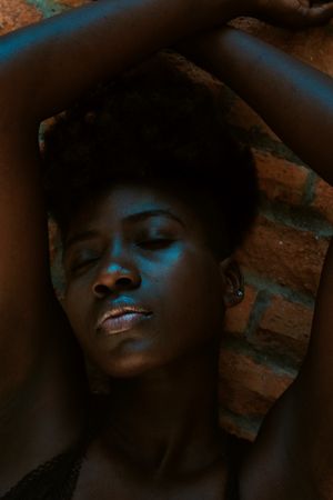 Young Black woman with eyes closed against wall