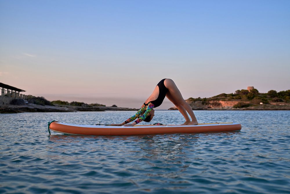 Young woman taking Adho Mukha Shvanasana pose on paddleboard