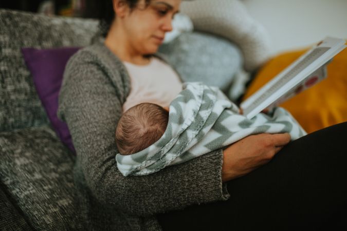 Mother reading a book while breast feeding her newborn baby