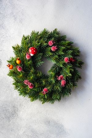 Top view of Christmas wreath with red berries on marble counter, vertical composition
