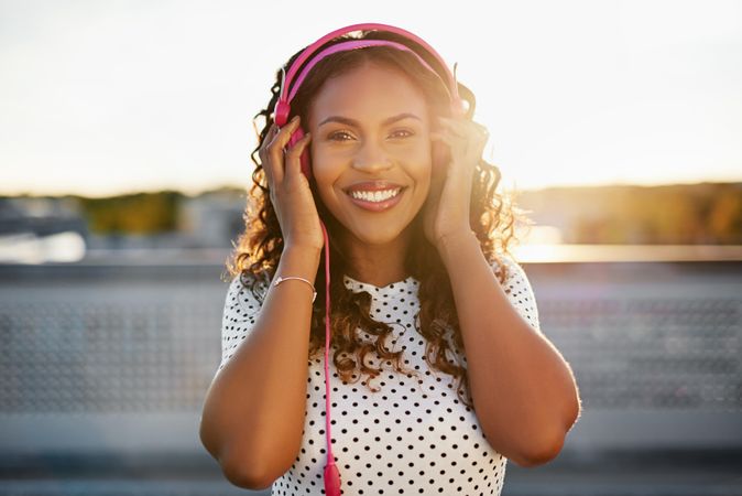 Smiling Black woman holding pink headphones on her head