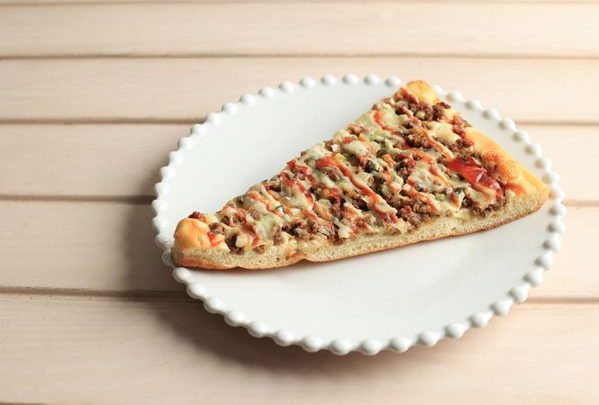 Slice of pizza with sauce drizzled on top on wooden table