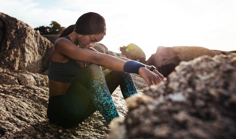 Young woman sitting rocks outdoors after her workout and looking down