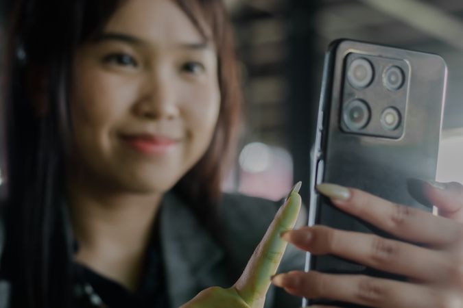 Asian woman interacts with mobile phone camera app, smiling soft