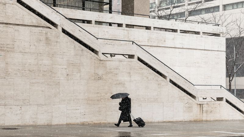 Person in dark outfit holing umbrella and walking near staircase