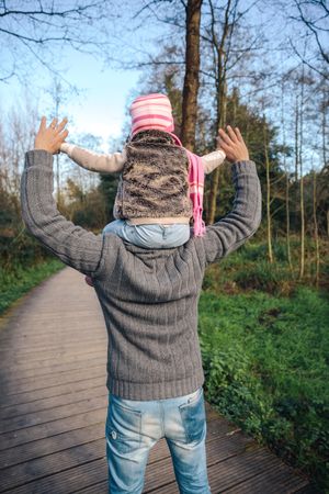 Back of father giving daughter ride on his shoulders in forest