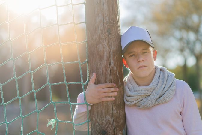 Portrait of a teenage male wearing a cap leaning on net