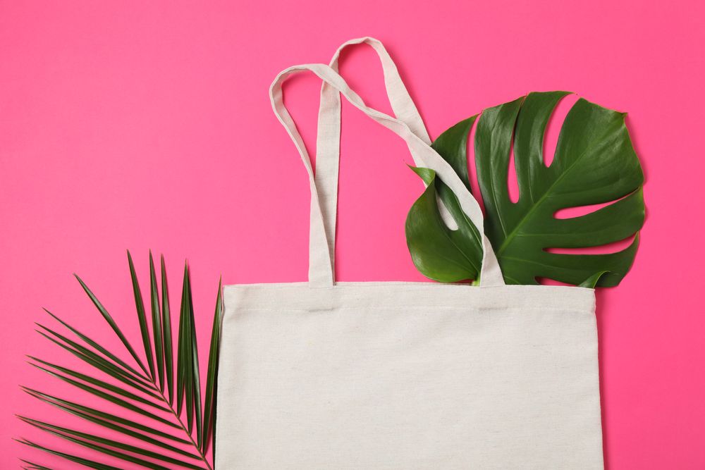 Eco bag and palm leaves on color background, top view