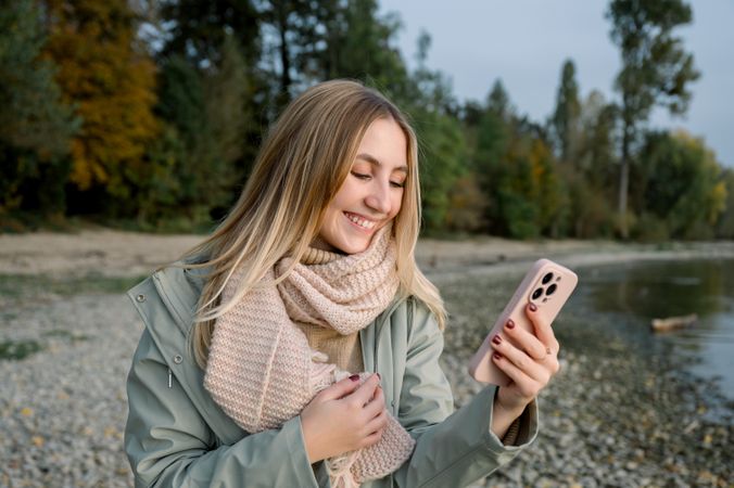 Smiling woman with smartphone near lake