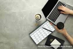 Top view of a person at a grey desk with calendar, laptop, cactus and coffee 5zMzN0