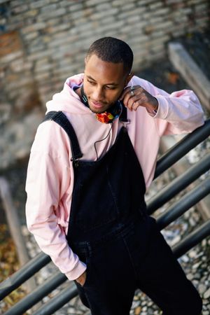 Male in overalls and pink hoodie leaning on railing of stairs outside