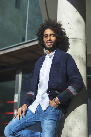 Black man in cardigan and jeans standing outside on sunny day