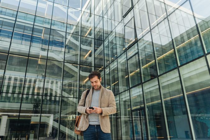 Smiling entrepreneur using smartphone outside office building
