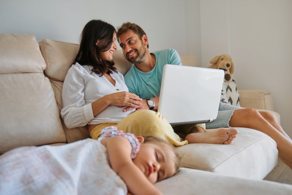 Smiling mother and father watching video on laptop near sleeping
