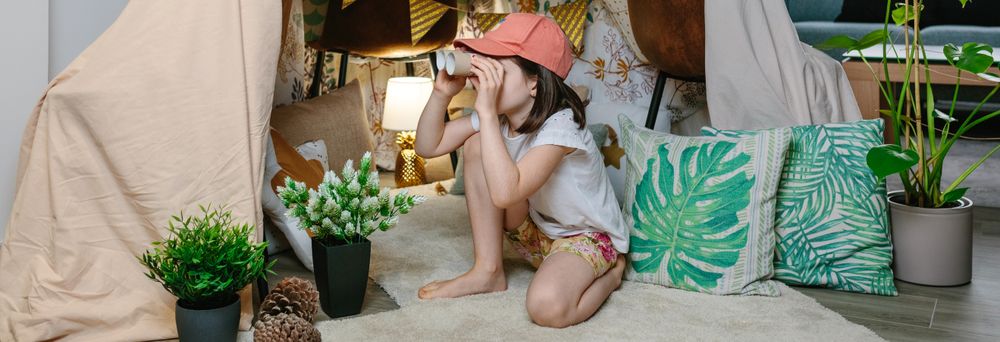 Girl playing with cardboard binoculars while camping at home