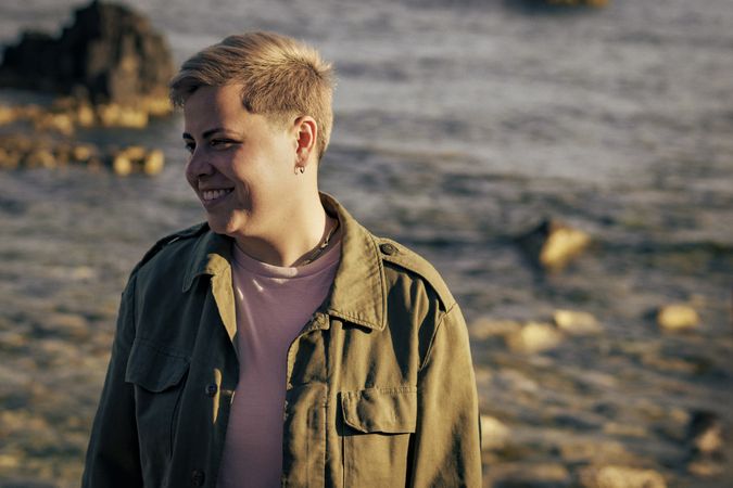 Happy non-binary person smiling at the beach during sunset
