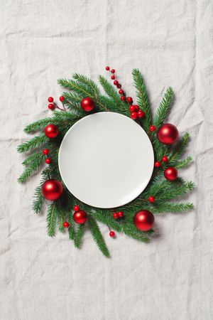 Top view of festive place setting of dinner plate with fir wreath and red baubles