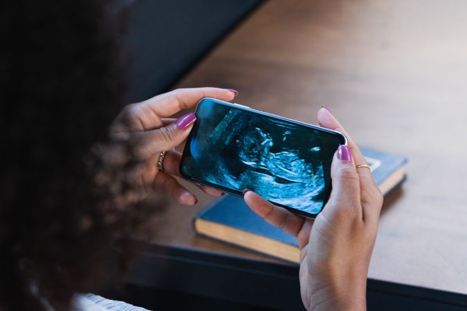 Black woman watching baby ultrasound picture on smartphone
