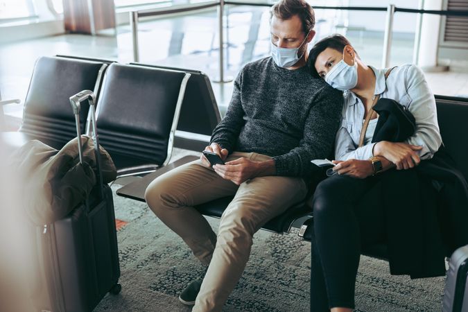 Couple with face masks sitting in waiting area at airport
