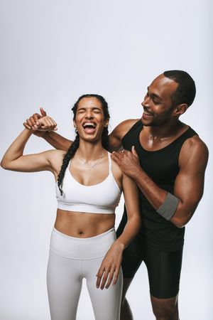 Playful woman flexing her bicep as male friend stands beside her