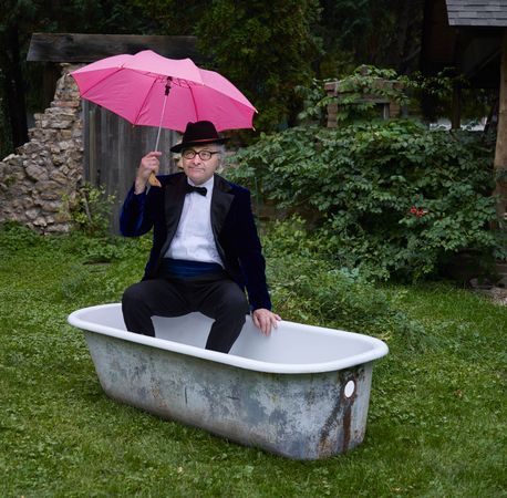 Gentleman with pink umbrella in a tub outside