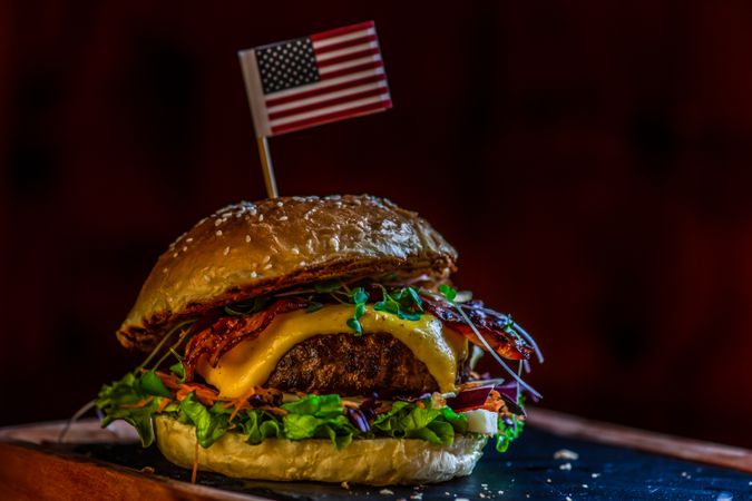 American hamburger with meat, cheese and different vegetables on dark rustic background topped with flag