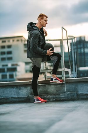 Side view of an athlete standing near a rooftop staircase and looking away