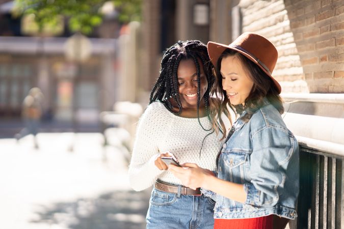 Female friends both smiling and looking down at a cell phone